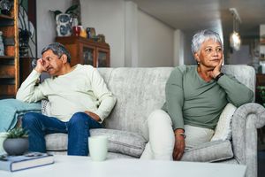 Upset couple sitting apart from one another on a grey couch 