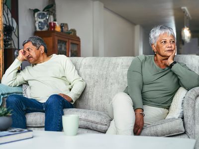 Upset couple sitting apart from one another on a grey couch 