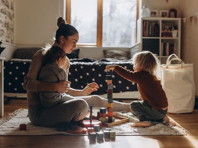 Young Mother playing with children while sitting on floor at home with wooden toys