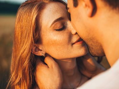 Close-up portrait of a freckled girl kissing her boyfriend while they are on an outdoor date. Wheat field. People lifestyle concept