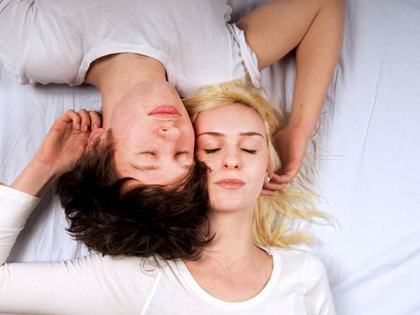 Young couple lying on white sheet, eyes closed, side by side.