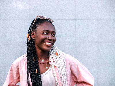 Young black braided woman smiling outdoors in the summer against gray background.