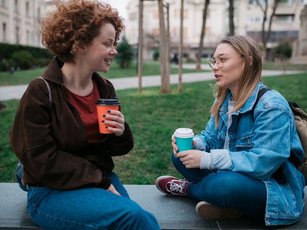 Side view of two happy female friends meeting in a city for a cup of coffee