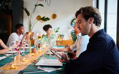 Young man distracted by a text on his mobile phone while sitting at a table with friends before an evening dinner party