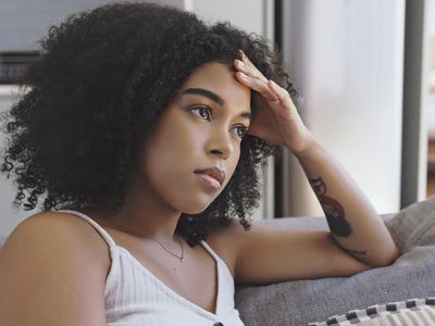 curly haired-person looking stressed, with tattoo on arm