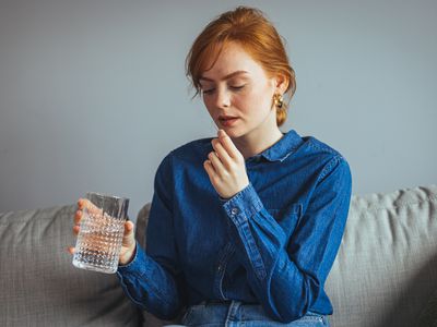 Young beautiful woman taking tablet with glass of fresh water. Close up of woman holding a glass of water and medication in her hand