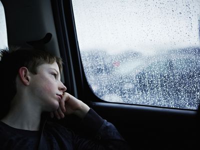 Young boy looking out rainy car window