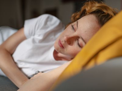 Close up view of a redhead young woman, dressed in casual clothes, lying on her side on a sofa in the living room of her house, looking away with sad face. Moment of loneliness and sadness.