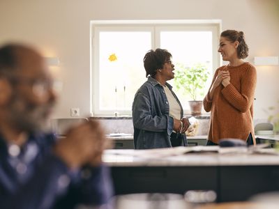 Woman with hands on chest talking to mother-in-law standing in kitchen at home