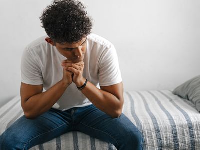 Young adult man sitting on bedroom thinking.