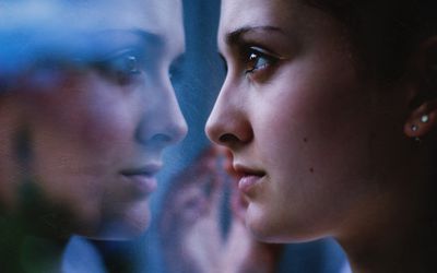 Woman's face close up, staring in mirror with reflection.