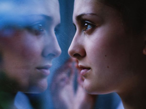 Woman's face close up, staring in mirror with reflection.