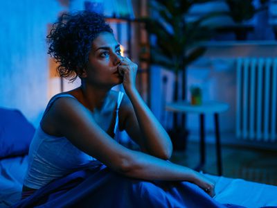 Young woman having insomnia while sitting on the bed at night in her bedroom.