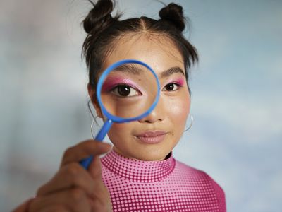 Teenage girl with magnifying glass against colored background