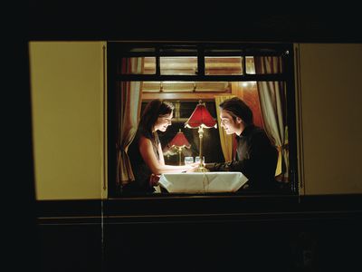 Young couple at table aboard train, exterior view, night