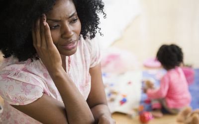 Frustrated mother rubbing her temples while child plays in background