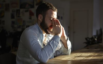 Young man sitting at kitchen table with hands on face