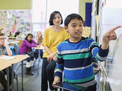 boy working with teacher on whiteboard in classroom