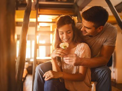 Affectionate man surprising his girlfriend with a carnation flower while sitting on staircase at home.