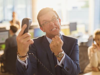 Furious businessman gesturing with fist at telephone in office