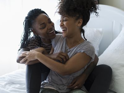 Lesbian couple relaxing on bed, hugging, laughing