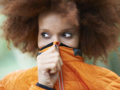 Portrait of woman covering mouth with coat looking away