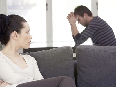 Young woman sitting on sofa, looking at distressed man at table