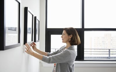 Woman, in her 40's, hanging picture in her apartment, straightening it to get it "just right" 