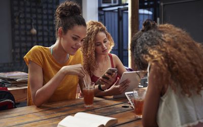 Young women sitting together on their devices