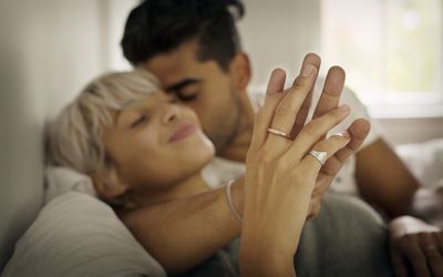 Affectionate young man kissing woman while holding hand in bedroom