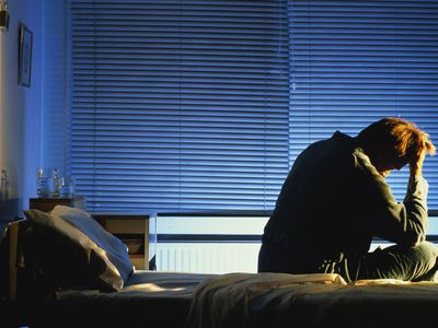 Distressed looking man sitting on hospital bed, head in hand, night