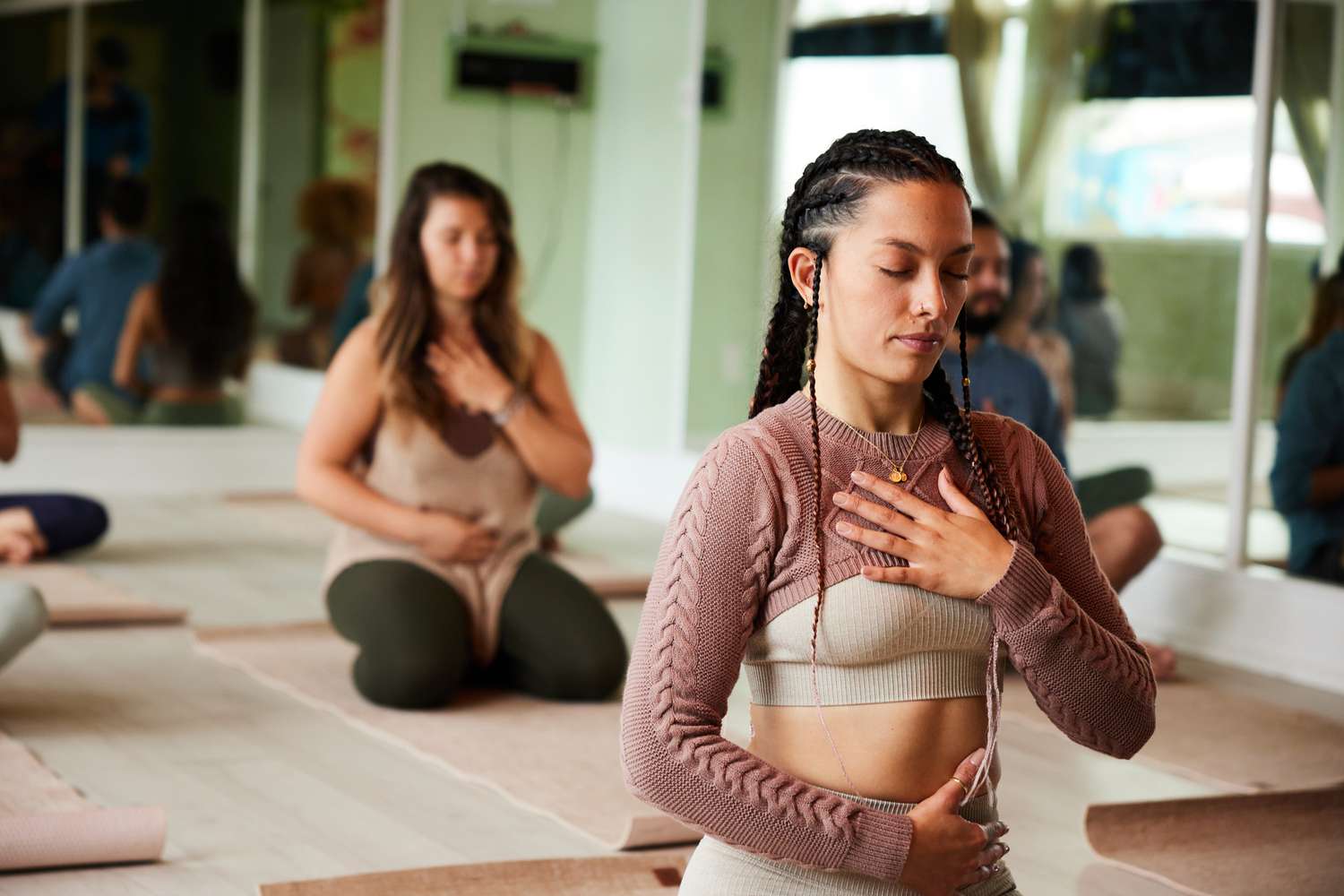 Young woman meditating with her eyes closed and touching her chakras during a yoga class