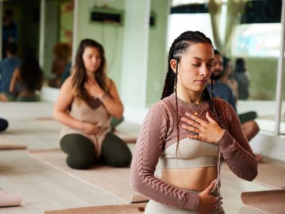 Young woman meditating with her eyes closed and touching her chakras during a yoga class