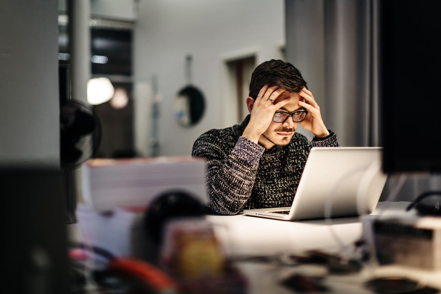 man holding head in hands looking at computer screen