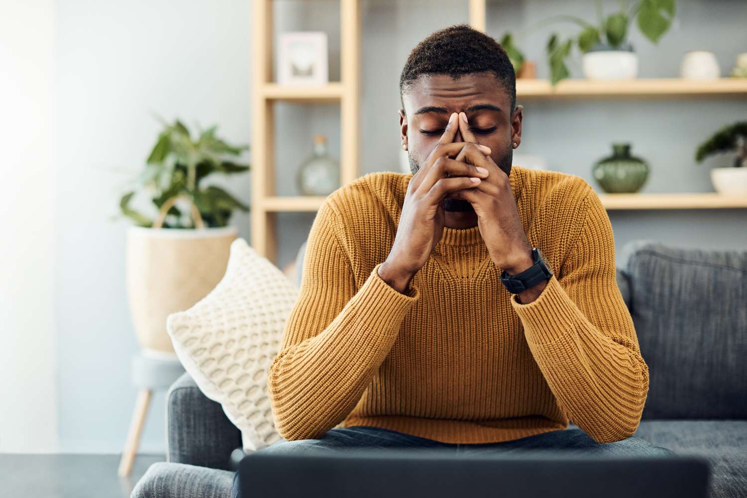 Young man looking deep in worry sitting on a couch at home