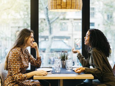 Two young smiling women sitting on a restaurant table