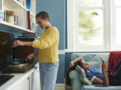 Woman playing music on turntable while partner is using mobile phone on sofa at home