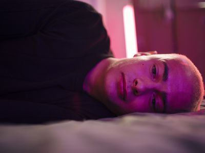 person lying on their side looking sad in pink lighting