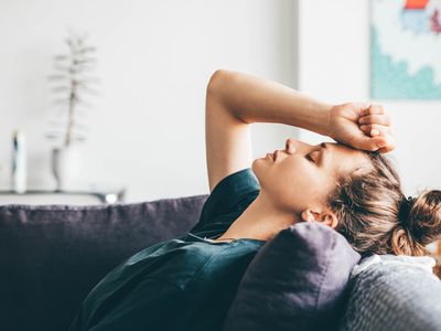 woman lying on the couch with her fist on her forehead looking tired.