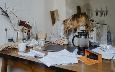 woman sitting at messy desk, slightly blurry with her head in her hands