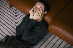 person lying halfway on the ground and halfway on the couch with hands covering eyes