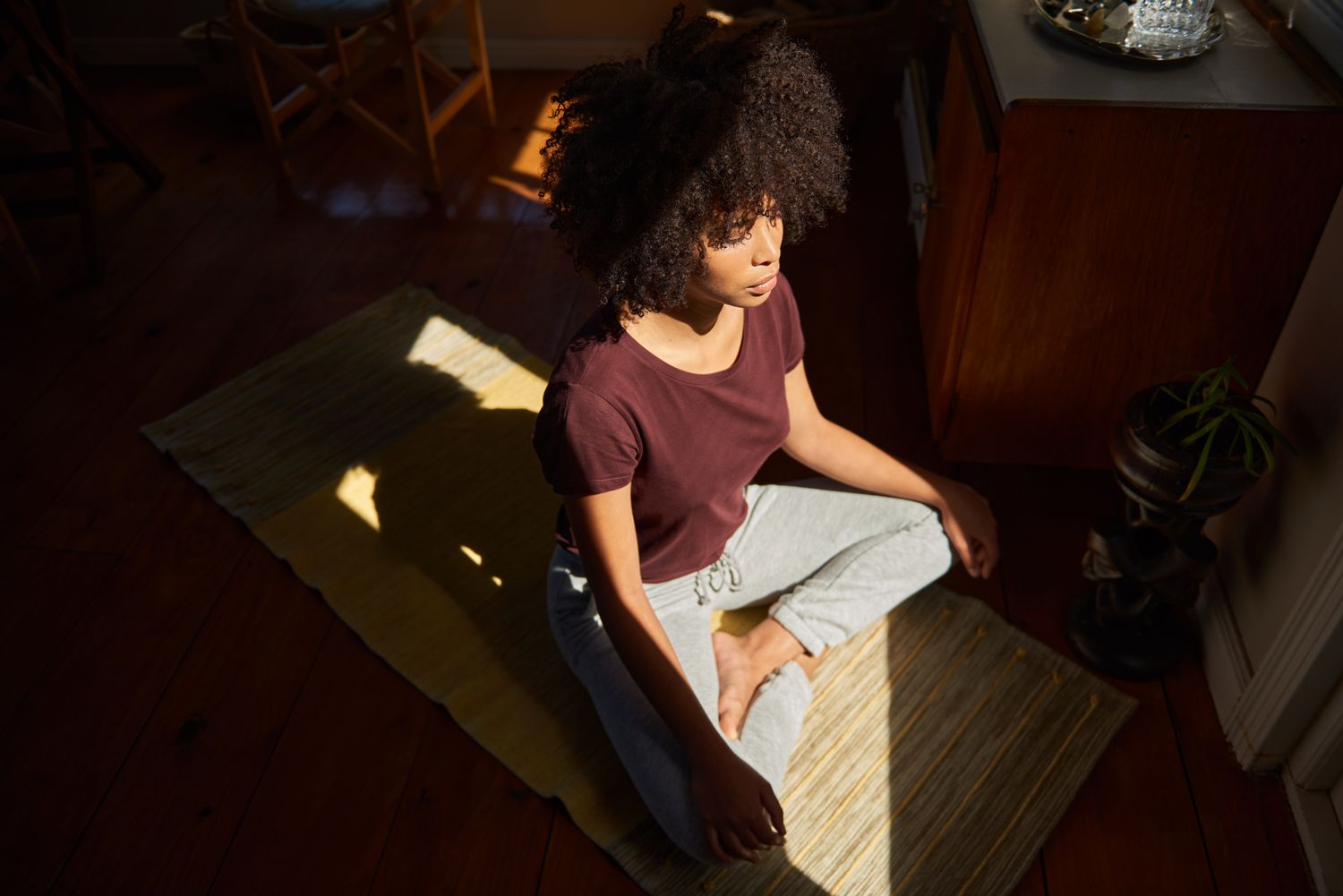 High angle view of a young African woman meditating in a ray of light on the floor of her living room