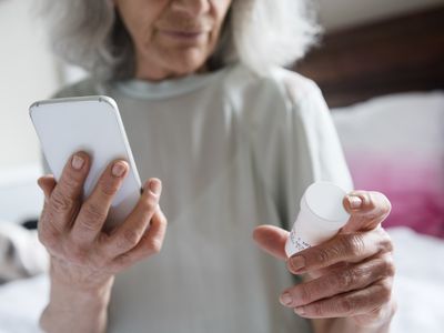 Older woman holding smartphone in one hand and pill bottle in another