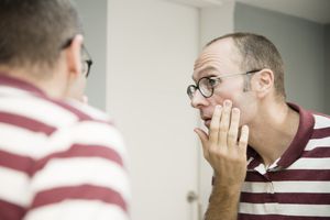 Over shoulder view of mature man looking at his face in bathroom mirror