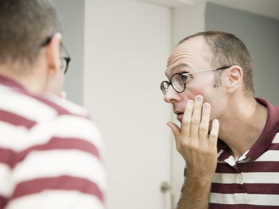 Over shoulder view of mature man looking at his face in bathroom mirror