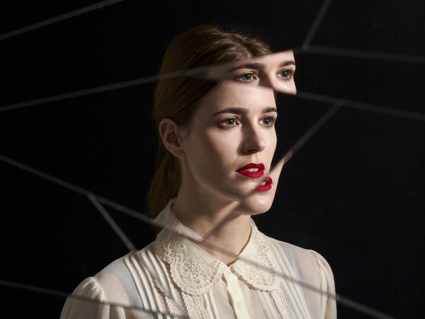 a straight-faced woman looking out against a black background as if through a broken mirror