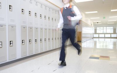 School boy (16-17) running past lockers in corridor