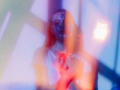 Stylish film looking portrait of pretty teenage girl with beads on her face and colorful flares around her posing with closed eyes