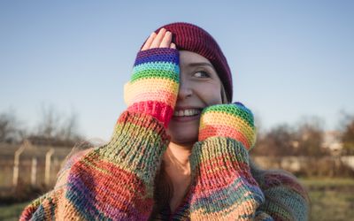 Smiling woman wearing rainbow gloves covering face with hands on sunny day