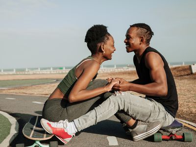 Beautiful young seated skater couple holding hands close 